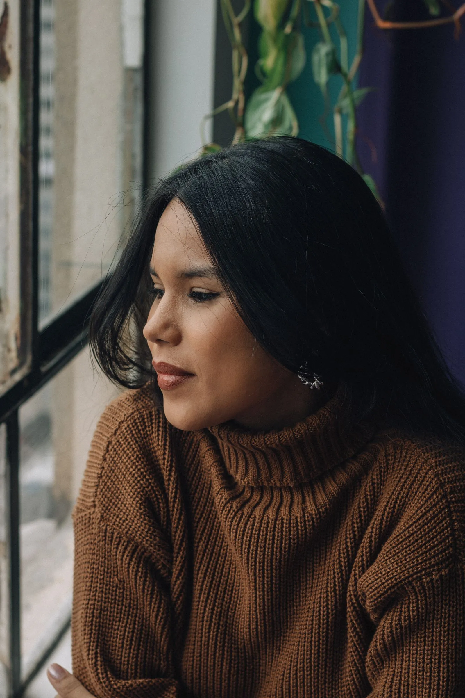 A woman in a warm brown sweater gazing quietly out a window
