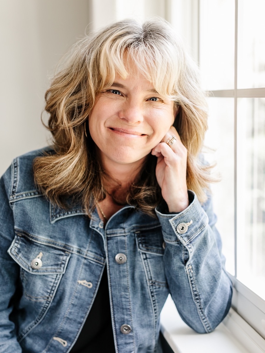A woman in her fifties with a warm, hopeful expression by a bright window