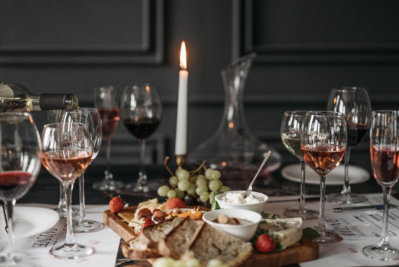A candlelit table set with glasses of wine, a cheese board, grapes, and bread