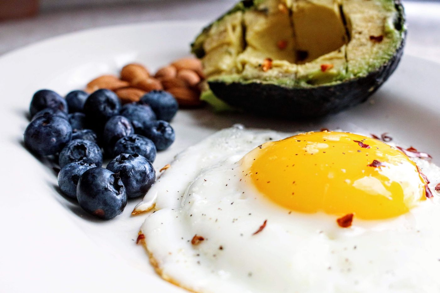 A plate with a fried egg, avocado, blueberries, and almonds